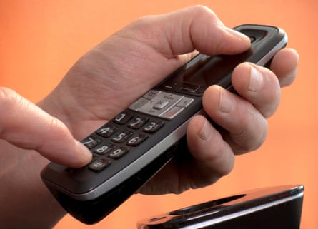 A man’s hand holding a hands-free landline telephone while pressing a number on the keypad to make a phone call.