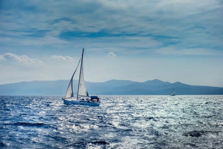 Yacht sailing in Adriatic sea with hilly rocky coast in the distance