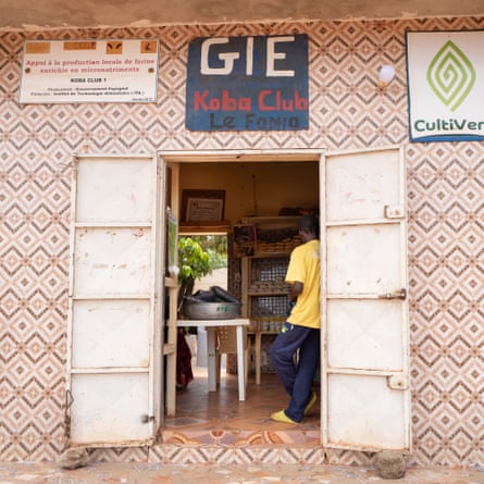 A man is seen through the metal doors of a simple shop with a tiled exterior