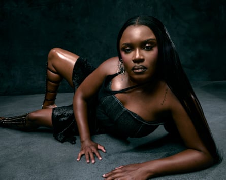 The singer Amaarae, lying on the ground leaning on her elbow, dressed in black