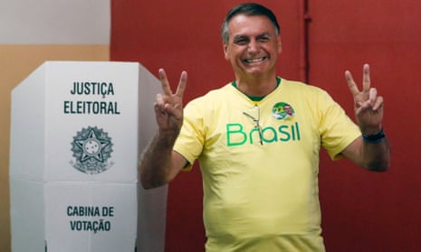 Jair Bolsonaro smiles and flashes the ‘victory’ sign as he stands next to a voting booth
