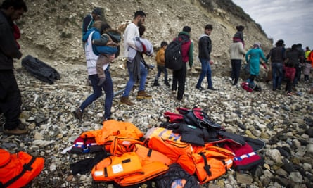 Syrian refugees walk past life vests after arriving on Mytilene beach, Lesbos, Greece