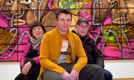 Mark Scofield seated in a group with his mother and father on either side of him in front of one of the large artworks in the gallery