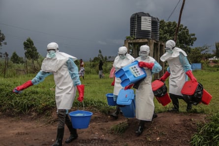 Medical staff wearing personal protective equipment carry blue buckets and crates of disinfectant.