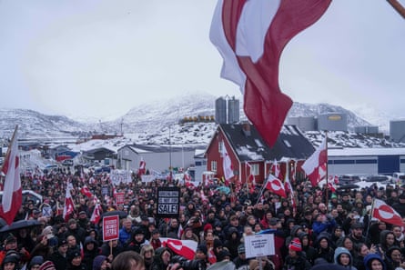 A crowd of protesters holding Greenland flags on a winter’s day