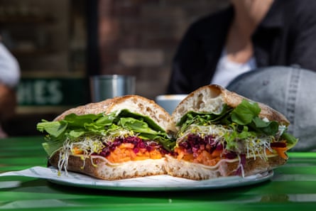 A sliced salad sandwich on a plate, placed on a green outdoor table under dappled sunlight