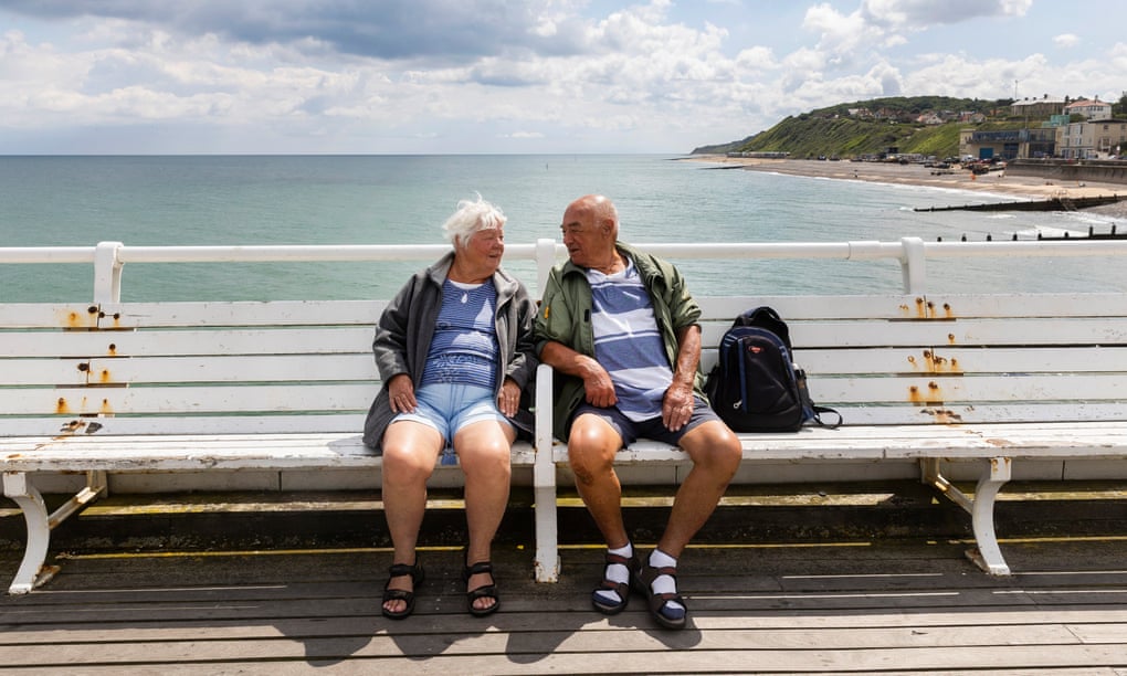 An older couple sit on a bench at Cromer, North Norfolk, in front of the sea.