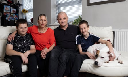 Clare Willsher sits on a sofa next to her husband with their two sons either side and a white dog being held by the boy on the right