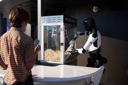 A robot scoops popcorn as a person waits at counter