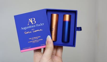 A hand holds up the augusinus bader lip balms in their in case