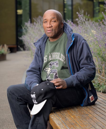 An older black man sits on a bench holding a baseball cap in his hand.