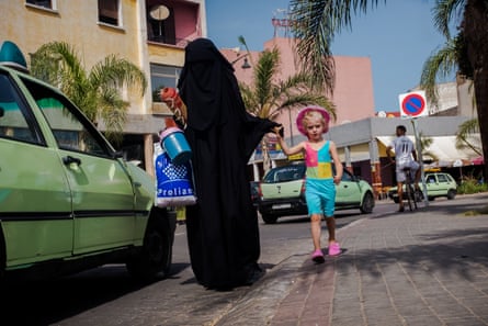 A woman in a black burqa walks past a child wearing colourful shorts and a vest