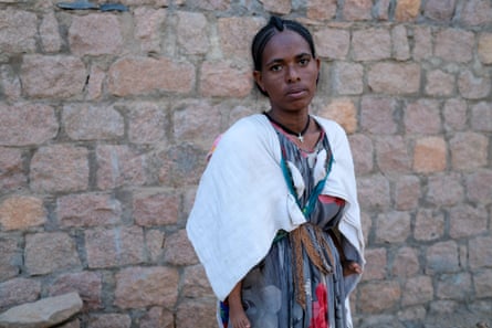 A woman in a white shawl standing against a wall