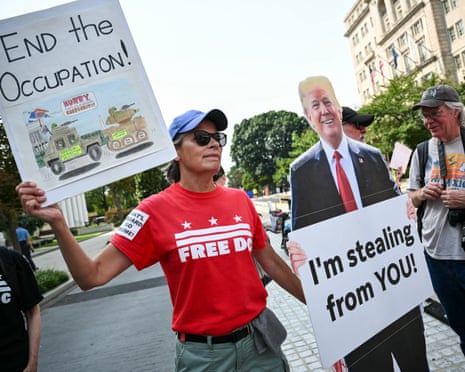 Demonstrators rally during a ‘Free DC’ protest in Washington DC to mark one year since Donald Trump deployed the National Guard into the city. Their placards read ‘End the ocucpation’ and Trump holding a sign that says ‘I’m stealing from you’