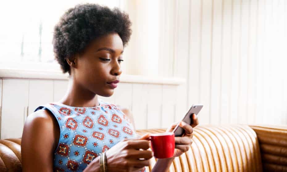 Woman on sofa with smartphone and coffee.