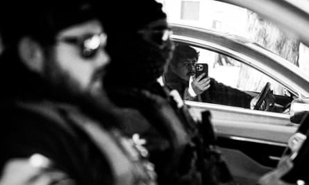 a black and white photo of a man pointing his phone camera at federal agents from his car