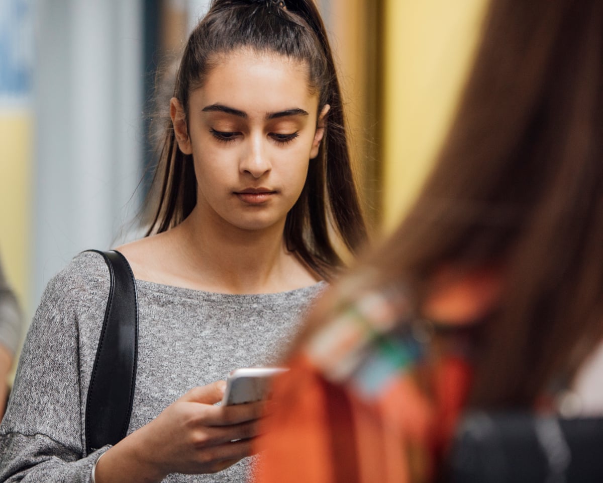 A female student walking down a corridor looking at her mobile phone.