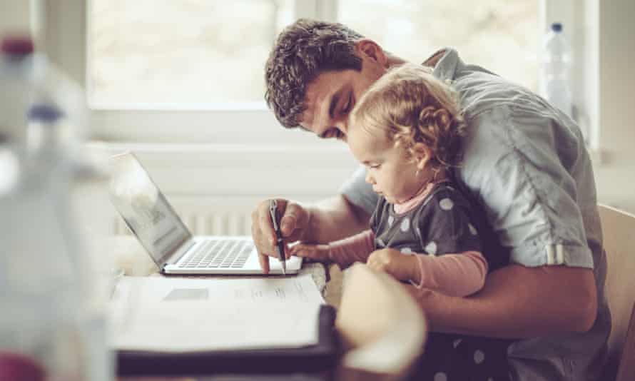 Man holding a toddler while working on a laptop