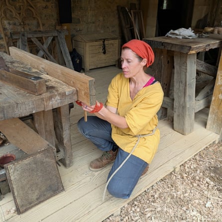 A woman in a yellow top, her hair in a red scarf, works on a thick plank of wood