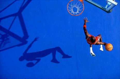 Michael Jordan jumping to dunk a basketball, his shadow visible on the blue floor below