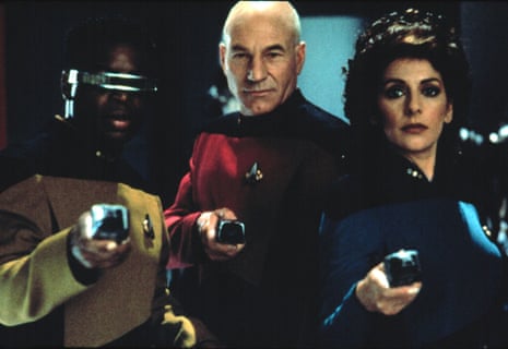 Three Star Trek crew members, including Picard, aim phasers forward with serious expressions