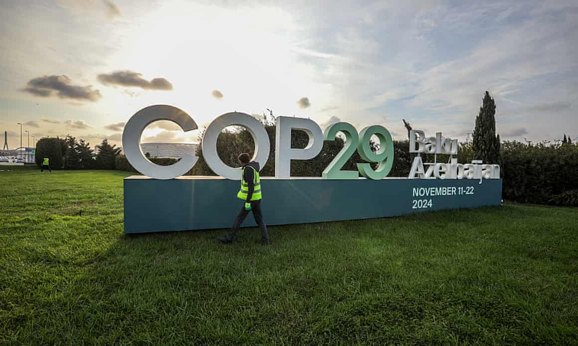 A worker walks past a Cop29 sign as the sun shines in the sky behind