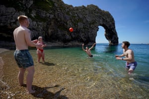 A group of friends enjoy a game of volleyball in the sea at Durdle Door, Dorset