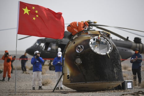 A person crouching on top of a capsule with the Chinese flag in the foreground
