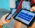 A person holds their phone next to an iPad prompting them to add a tip