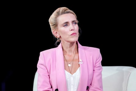 A woman in a pink jacket sits on stage