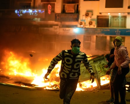 A young man runs past a burning police car