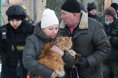 A woman holds a cat while an officer and other local residents are stood behind her
