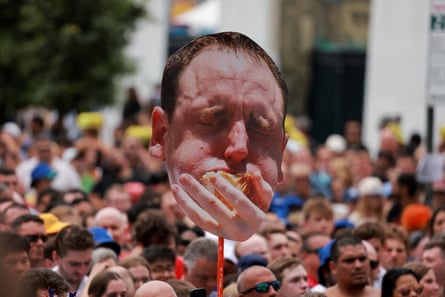 a cutout banner held above a crowd shows a man forcing a hotdog into his mouth