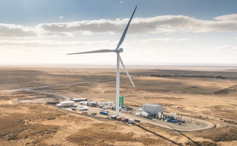 An aerial view of a small industrial complex in desert-like landscape with a large windmill