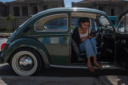 A VW Beetle with a young woman sitting half in, half out of the car
