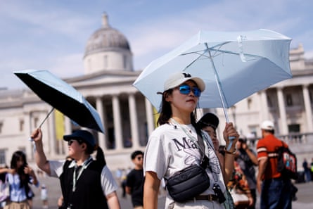 People use umbrellas to shelter from the sun as they visit Trafalgar Square in central London.