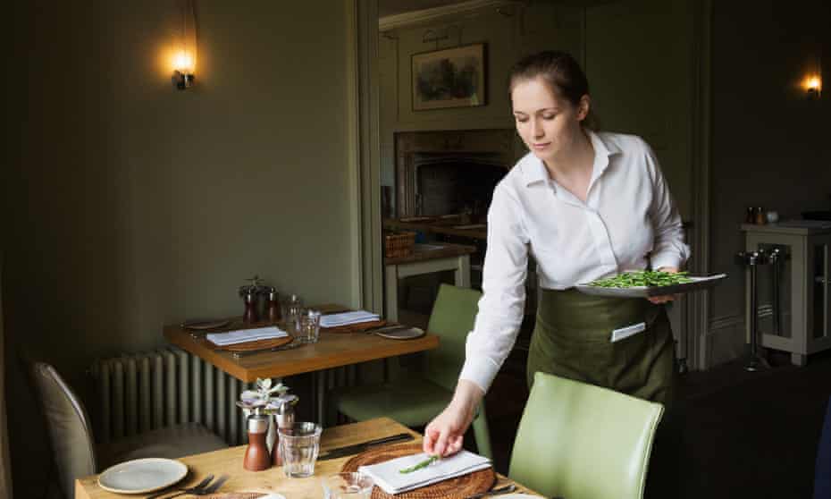 Woman wearing apron setting table in a restaurant.