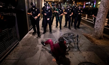 A woman falls off her bicycle as police officers prevent protesters from entering a street in Los Angeles