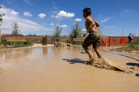 A young boy runs through a large muddy puddle.