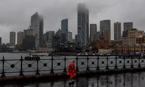 Man in orange rain coat walking past Sydney CBD skyline hidden behind fog
