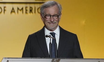 Steven Spielberg stands at a podium against a gold background.