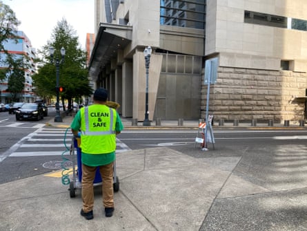 Urban high rise with person in neon green vest pushing wastebasket on wheels.