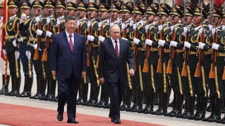 Vladimir Putin and Xi Jinping walk down a red carpet past soldiers.