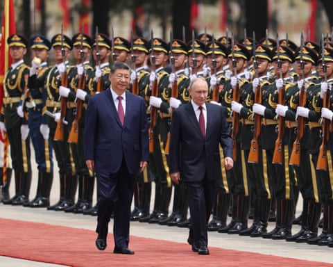 Putin and Xi walk past an honour guard of soldiers holding rifles with bayonets on a red carpet