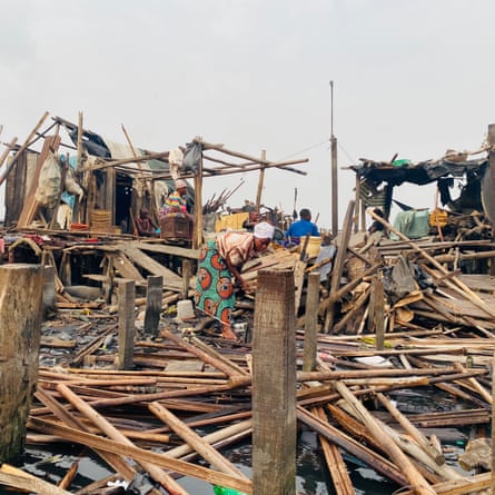 ‘They told us to leave. They didn’t tell us where to go’: the demolitions destroying homes and lives in Lagos A woman in a wrap dress lifts an armful of planks from the destroyed remains of a house.