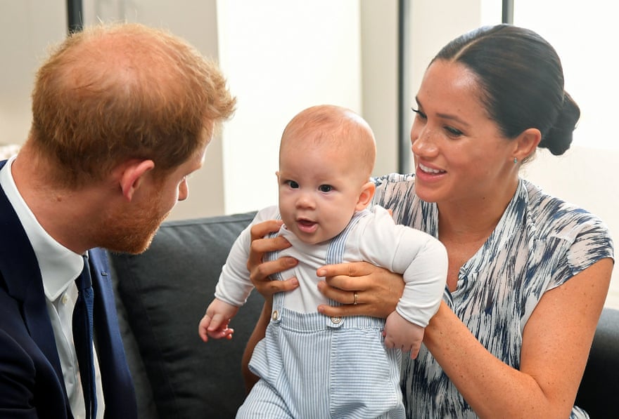 Prince Harry and Meghan sit on a couch as Meghan holds their son Archie.