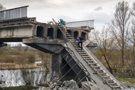Local residents on Tuesday climb a ladder to a bridge partially destroyed in the Kukhari village near Kyiv.