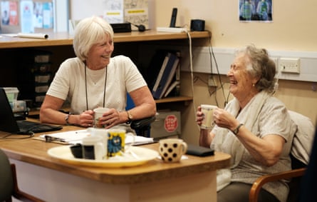 Sue Harris and Marie Wragg laughing together sitting at a table drinking tea in a library