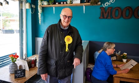 Gordon Birtwistle smiling while wearing a yellow rosette and leaning against a booth in a cafe