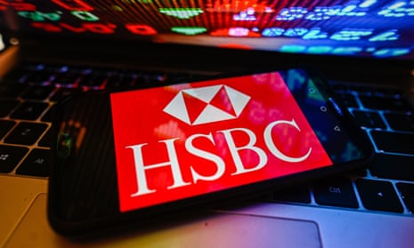 HSBC logo on a smartphone with stock market percentages on a laptop.